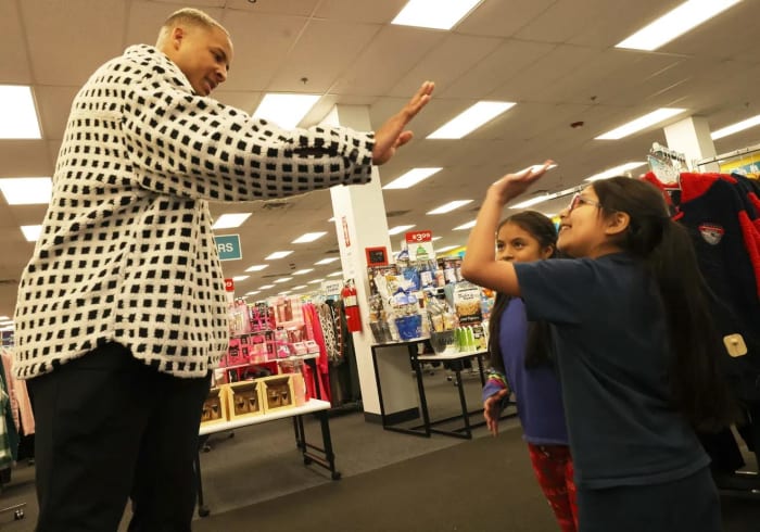 Customers Jhoanna Castro, 10, center, and Evelyn Chimbay, 7, get a high-five from New England Patriots tight end Pharaoh Brown at a surprise holiday payoff event at Brockton Citi Trends on Tuesday, Dec. 12, 2023.